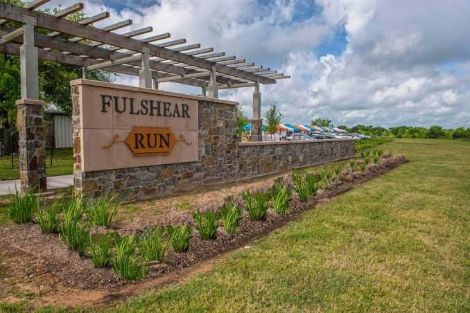 Fulshear Run monument sign beneath a wooden pergola, with pool furniture in the background