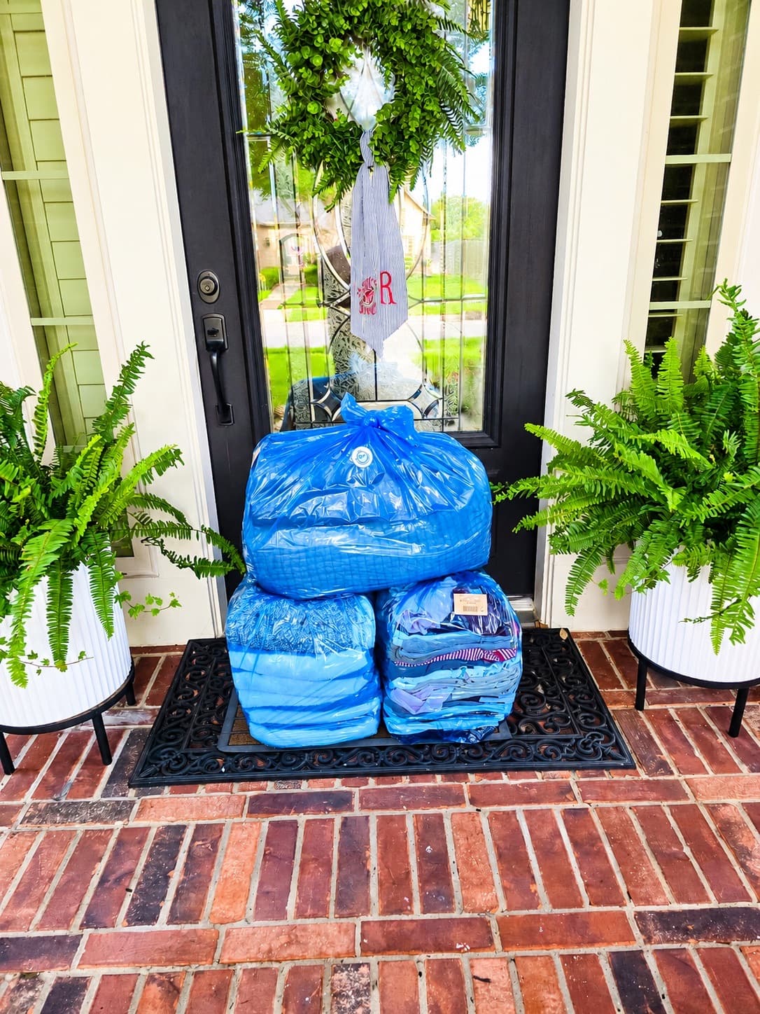 Bagged laundry ready for pickup on a doormat between potted ferns