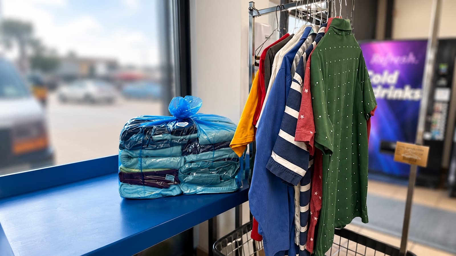 A wrapped wash & fold bundle on the counter next to a rack of hanging garments