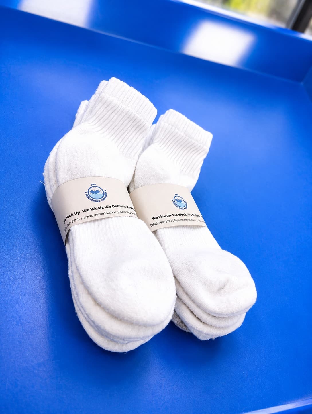 A folded pair of white socks banded with a Fry Washateria, Alterations & Cleaners sleeve
